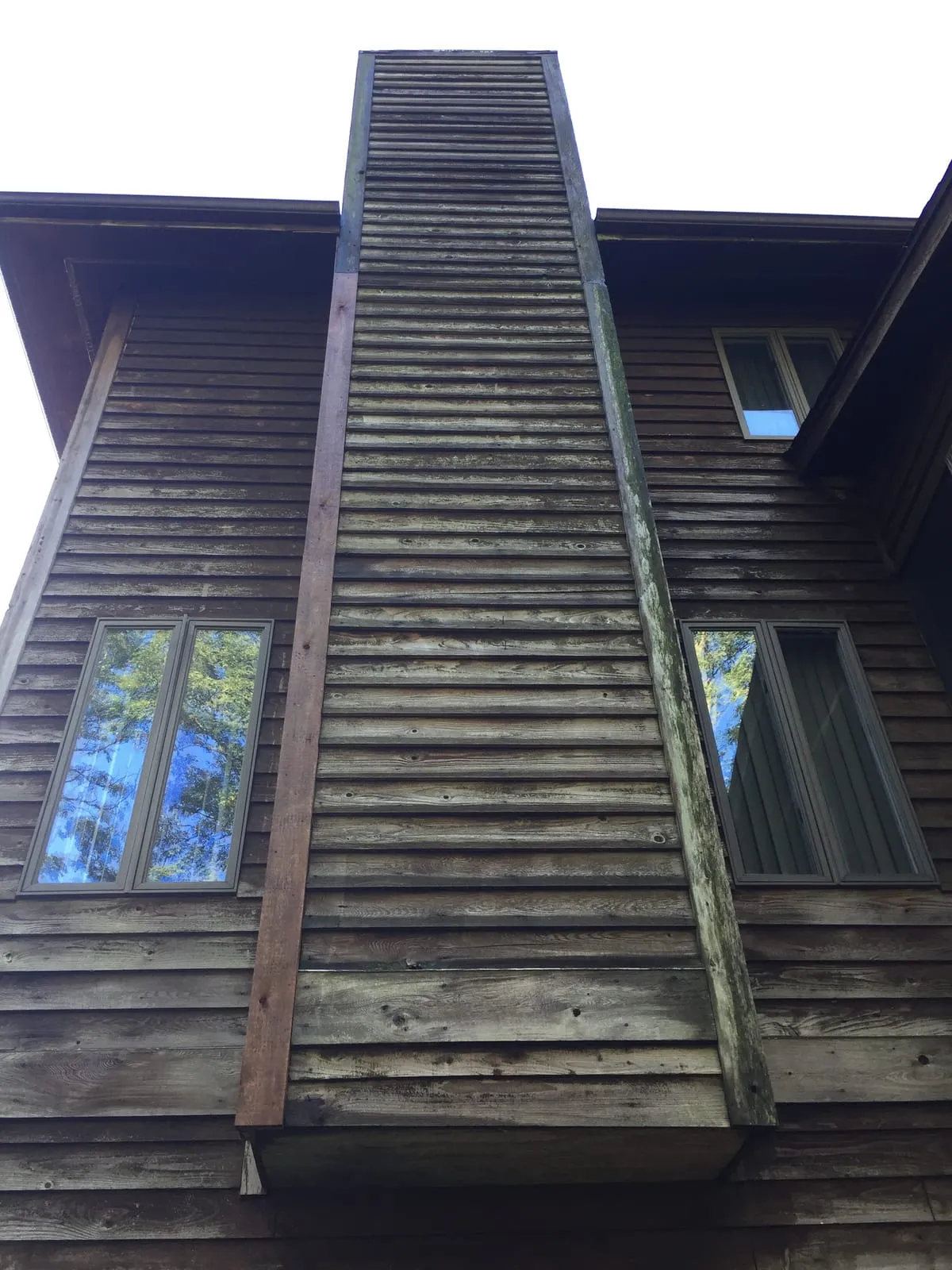 Tall weathered wooden chimney chase on a wood-sided house