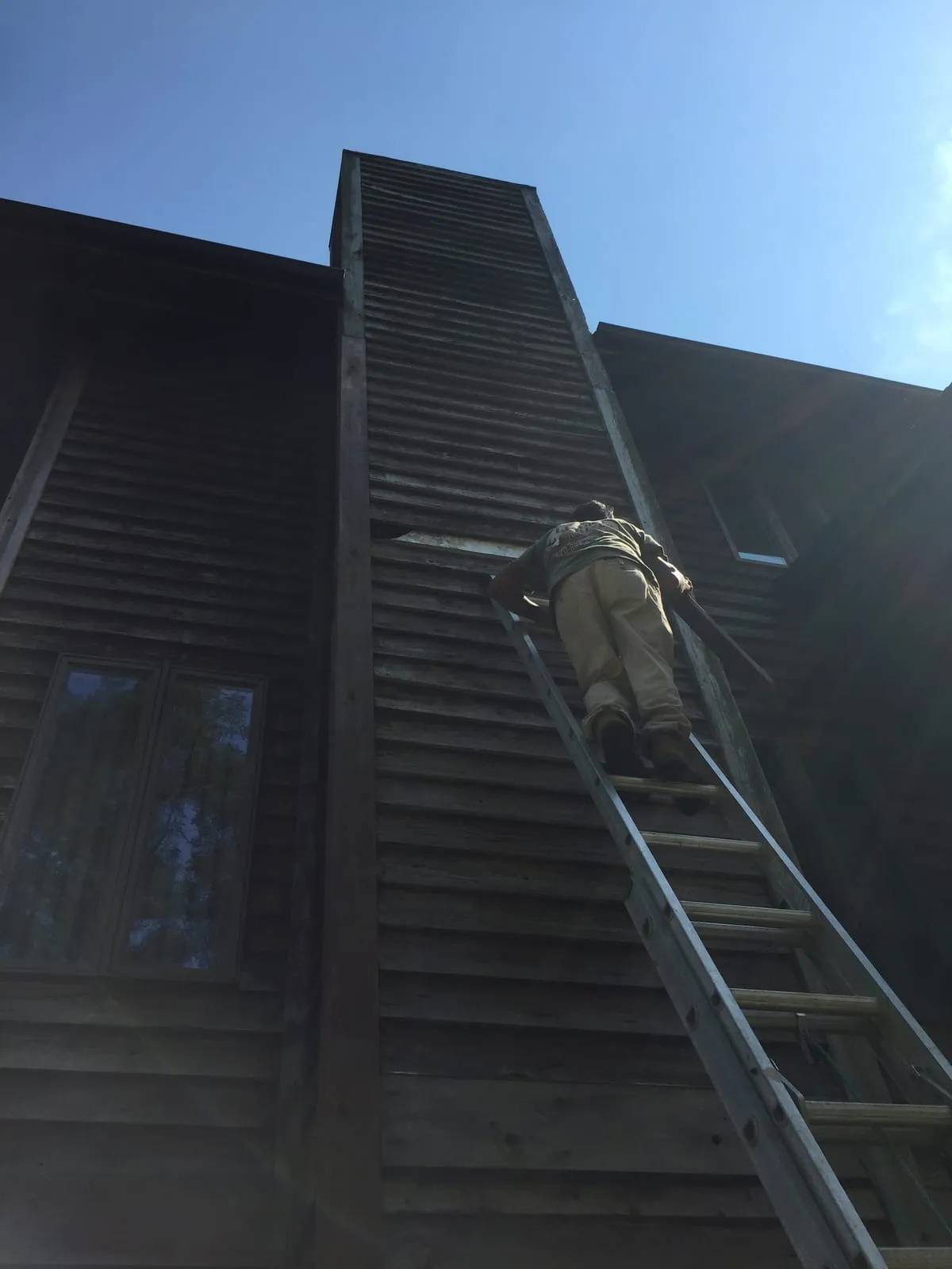Technician on an extension ladder inspecting the top of a tall wooden chimney chase