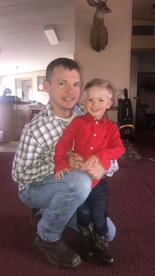 Chris Griffith kneeling indoors beside a smiling young boy