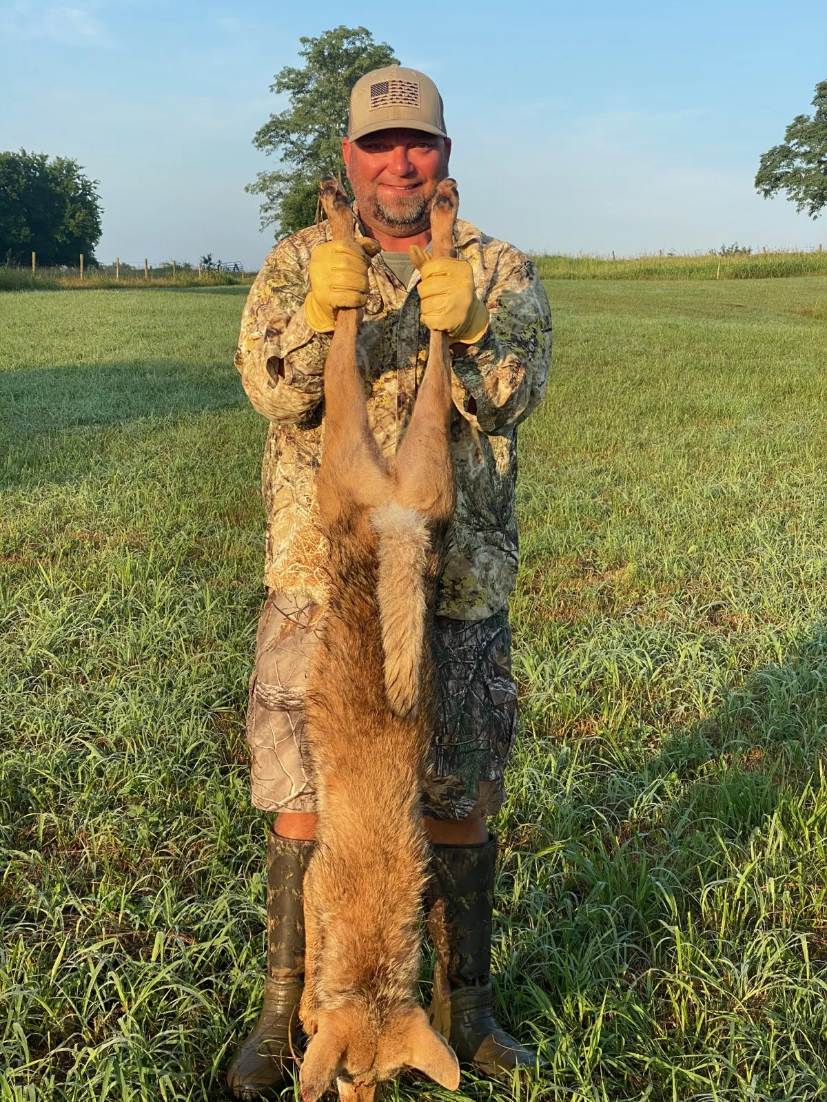 Jason Sparrow in camouflage holding a coyote in a grassy field