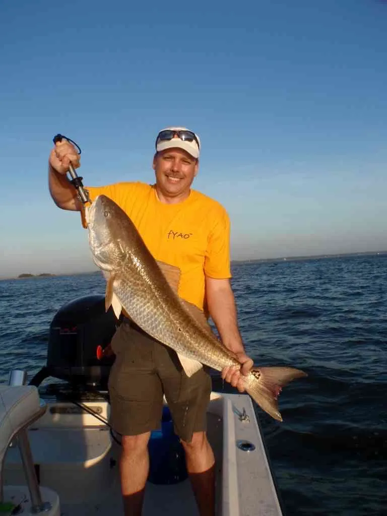 Jonathan Gassett smiling on a boat, holding a large fish he caught