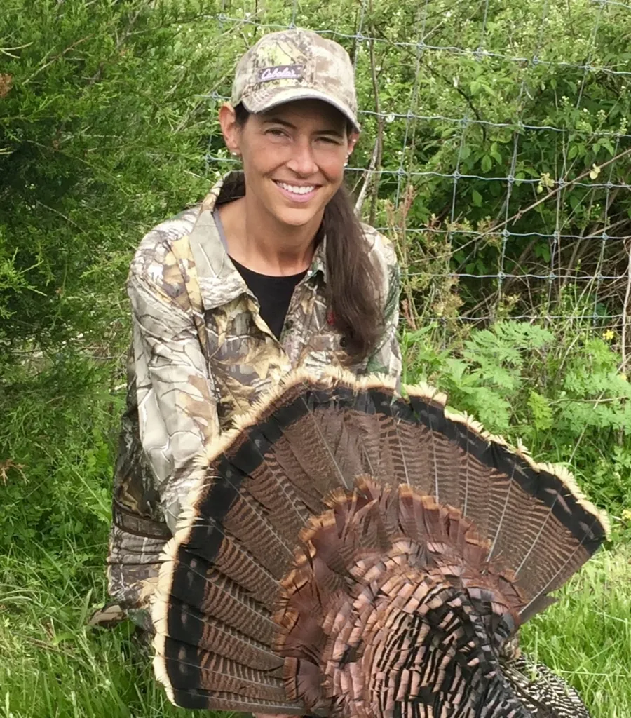 Kristie Blevins in camouflage, smiling behind the fanned tail of a wild turkey
