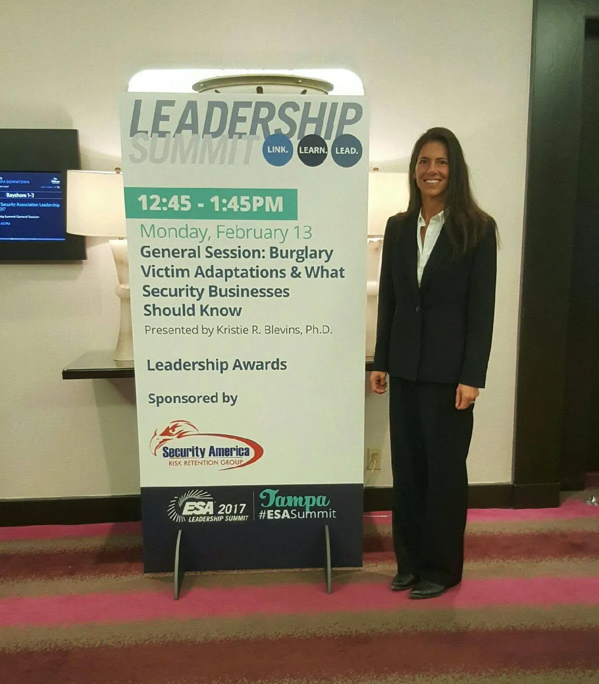 Kristie Blevins standing beside a tall Leadership Summit conference sign listing her general session presentation