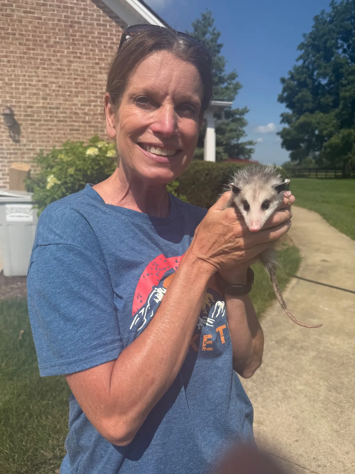 Tanya Clark smiling in the sunshine, holding a young opossum in both hands